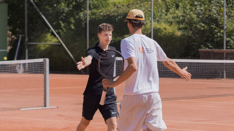 Two adult tennis players high-five on a clay court