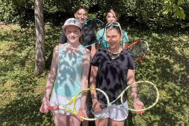 Vier Mädchen stehen vor einer grünen Wiese mit den Tennisschlägern in den Händen für ein Teamfoto.