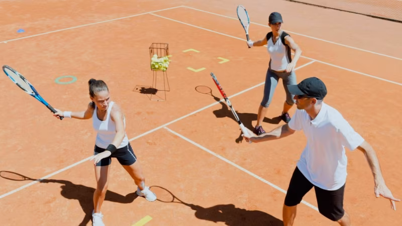 Adults playing tennis during a group training session on a clay court