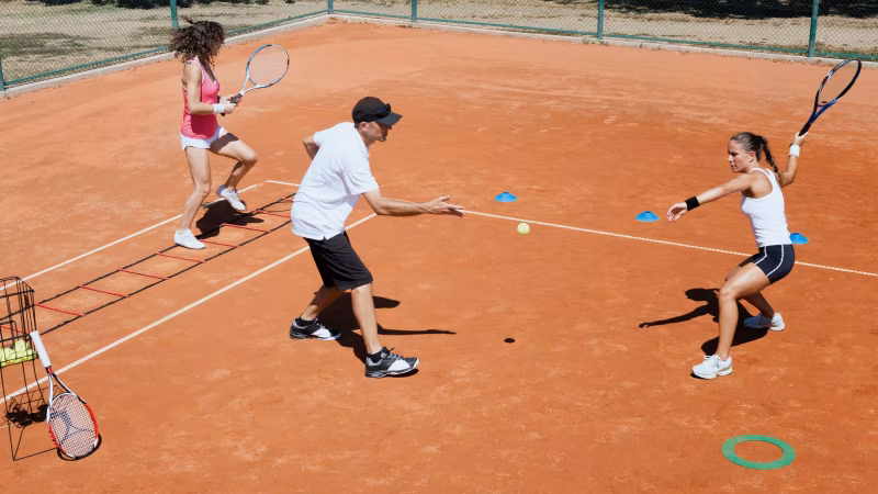 Adults practicing tennis on a clay court with a coach